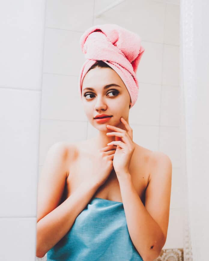 Young beautiful woman looks and touches her face in the mirror in the bathroom